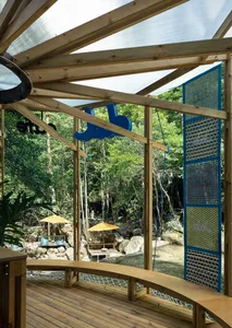 A wooden gazebo with a glass roof provides an outdoor restaurant seating area surrounded by nature.