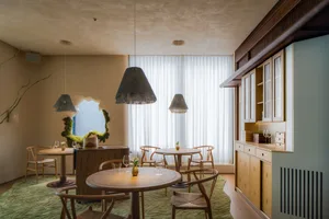 Modern restaurant interior with wooden tables, fabric curtains, and a window showcasing the outdoors.