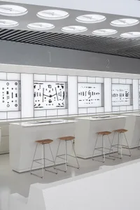 Industrial retail store area with metallic and wooden displays, white plaster counters, and stools.