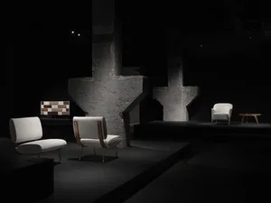 Minimalist furniture display with concrete columns, fabric upholstered chairs, and a geometric table in a black background se