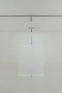A minimalist glass floating object installation art piece mounted on a white wall.
