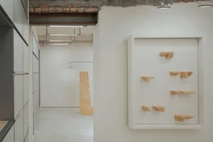 A minimalist office space with wooden columns, white walls, and an industrial ceiling beam.