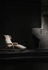 A minimalist chaise lounge with white fabric upholstery in a dark room setting.