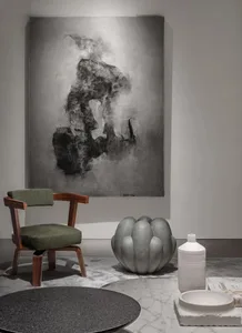 A minimalist interior design featuring abstract art on concrete walls and a wooden chair with green cushions.