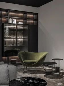 A modern living room with a green velvet armchair, marble side tables, and glass shelves.