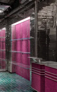 Modern retail space with metallic texture backdrop, glass shelves, and pink textile elements