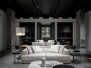 A minimalist living room with a white sofa, dark brown and orange chairs, and black and white coffee tables.