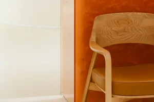 A modern wooden chair with orange cushions against an orange background.