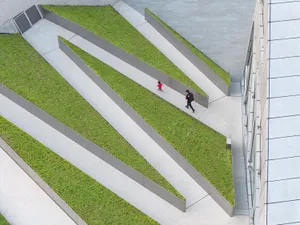 A modern urban green space featuring a green roof with concrete pathways and green grass bordered by metal frames.
