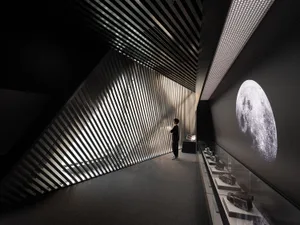 一位人士站在金屬牆面前，牆面由傾斜的金屬條組成，展示復古相機與大型月亮圖像。