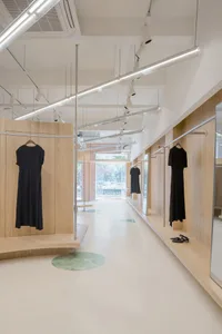 A clothing shop interior featuring minimalist design with wooden walls, glass doors, and concrete floor.