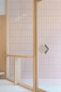Modern minimalist bathroom with light pink square tiles on the walls and floor, framed by wooden accents.