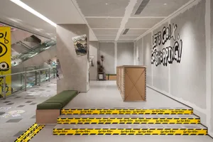 A modern shopping center interior with concrete floors and yellow warning tape on a flight of stairs.