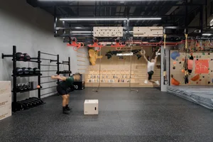 People exercising in a modern fitness center with a variety of equipment and climbing walls.