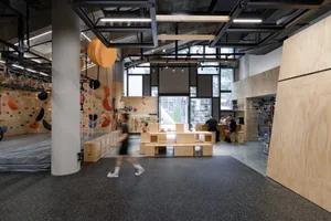 A spacious interior featuring an industrial climbing wall with colorful grips, surrounded by a modern, minimalist design with