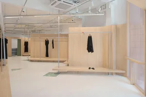 Modern minimalist retail display space featuring wooden and metal surfaces and concrete flooring, with clothing racks and sto