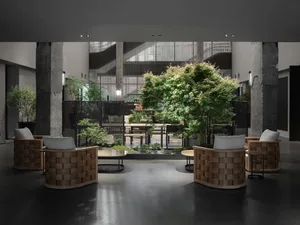 A spacious modern interior lobby with concrete floors, trees, and seating areas.