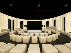 Circular arrangement of fabric-covered seating in a conference center with a stage and media equipment.