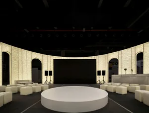 A minimalist conference room with a round, white platform at the center, surrounded by upholstered seating and concrete walls