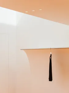 A minimalist clothing store display featuring a black garment hanging on a metallic rod against a light pink and white wall.