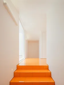 Modern minimalist staircase featuring bright orange tiles on the steps, against white walls and ceiling.