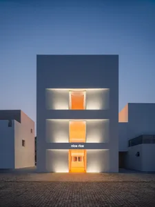Modern minimalist building with white concrete exterior at dusk, featuring illuminated windows and signage.