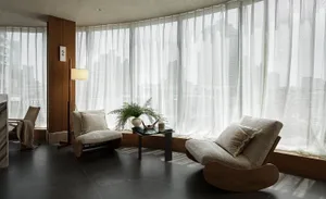 A minimalist living room with a modern, cozy aesthetic, featuring fabric and wood materials, and large windows with sheer cur