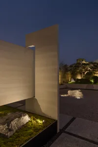 A minimalist residential courtyard featuring concrete surfaces, stone elements, and strategically placed lighting.