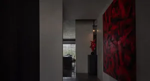 A modern dining room with a concrete minimalist design featuring a bright red artwork and a red sculptural vase.