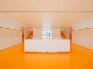Modern indoor lobby featuring orange-tiled floors and white concrete walls.