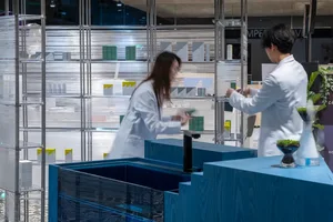 Two people in white lab coats working in a modern office with glass walls.