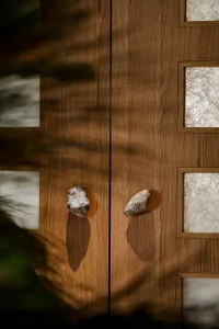 Close-up of wooden double doors with stone handles and frosted glass panels.