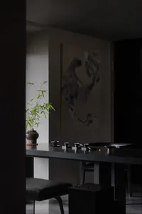 A minimalist interior space featuring a black wooden table with green plants and tea cups.
