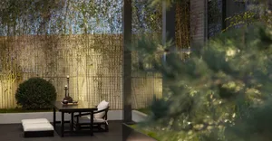 A minimalist outdoor dining area featuring bamboo plants, a stone table, and glass candle holders.