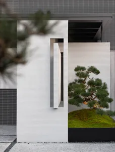 A modern minimalist outdoor space featuring concrete elements with a bonsai tree in a planter. Semicircular walls and curved 