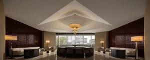 A modern hotel lobby features marble and concrete materials with a central dining table and seating areas.