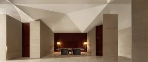 A spacious hotel lobby with minimalist design, concrete walls, and geometric ceiling.