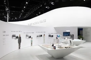 An indoor exhibition space showcasing audio technology products and materials, featuring a white curved wall and a display ta