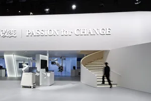 A minimalist exhibit hall with light concrete walls and a white spiral staircase.