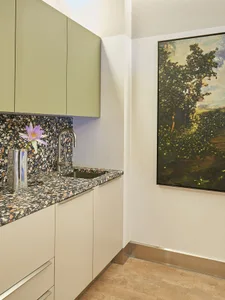 A minimalistic kitchen featuring a terrazzo countertop with a single purple flower in a vase.