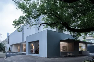 A minimalist concrete building with large glass windows and a tree in the foreground.