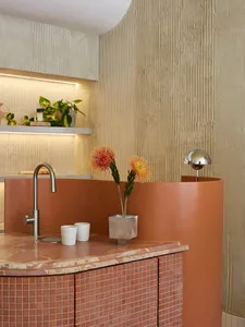 A modern bathroom featuring ceramic tile flooring and a terracotta-colored sink counter with a stainless steel faucet and pot