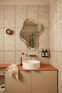 A modern bathroom featuring a unique patterned wall with a circular mirror, white sink, and peach-colored countertop.