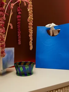 A blue decorative object with a white ribbon on a surface with dried flowers hanging in the background.