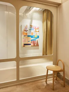 現代室內空間，牆面展示抽象藝術作品，搭配木質椅子與霧面玻璃面板。