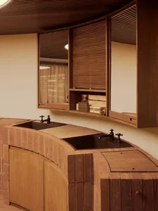 A modern kitchen with wooden cabinets and countertops, featuring a double sink and a shelf with storage items.