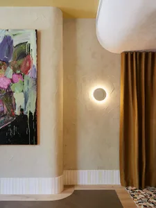 A modern residential interior with a textured wall, a circular wall lamp, and a gold curtain.