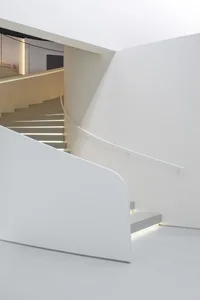 A sleek, modern interior space with white concrete walls and stairs illuminated by hidden lighting.