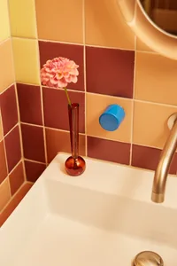 A bathroom scene featuring colorful ceramic tiles with a pink flower in a red vase.