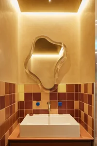 A minimalist bathroom featuring ceramic tiles with a mix of earthy tones and a unique, abstract-shaped mirror.
